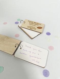 two wooden tags with writing on them sitting next to confetti covered tablecloth