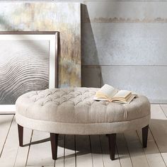 a round ottoman sitting on top of a hard wood floor next to a framed painting