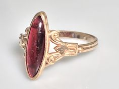 Very pretty antique ruby navette ring from the Victorian era in 10K yellow gold. This lovely ring features a marquise-cut cabochon ruby in a classic late Victorian oval bezel mount. The ruby is a simulated ruby, typical of the era, and measures 16.4x6mm and appears to be original to the ring with no chips or cracks and only very minimal age related wear. Beautiful. classic late Victorian-Art Nouveau detail to the sides. The shank is a beautiful handmade double shank and is solid all around. Ring Antique Marquise Rings For Formal Occasions, Antique 14k Gold Marquise Ring, Oval Ruby Ring In Art Deco Gold Style, Vintage Ruby Oval Cabochon Ring For Wedding, Vintage Oval Cabochon Ruby Ring For Wedding, Vintage Marquise Cut Ruby Ring, Vintage Oval Cabochon Ruby Wedding Ring, Vintage Marquise Ruby Wedding Ring, Antique Marquise Jewelry