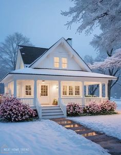 a white house with flowers in the front yard and snow on the ground around it