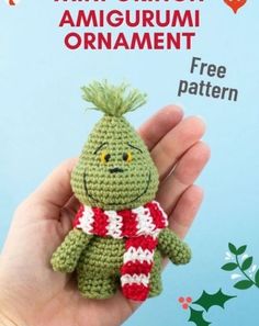 a hand holding a small crocheted green stuffed animal with a red and white striped scarf