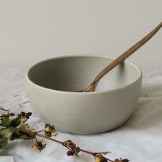 a white bowl with a spoon in it next to some dead flowers on a table