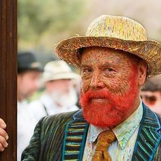 a man with red hair wearing a straw hat and tie next to a painting of an old man