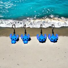 four little blue toy elephants are on the sand by the water's edge, with hooks attached to them