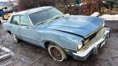 an old blue car is parked in the mud