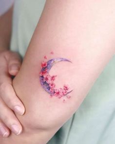 a woman's arm with pink flowers and a crescent shaped tattoo on the wrist