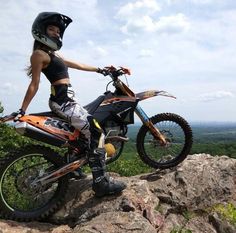 a woman is posing on top of a mountain with her dirt bike in the foreground