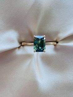 a ring with a green stone on it sitting on a white cloth covered pillowed surface