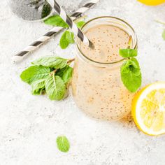 a glass jar filled with liquid next to two lemons and some minty leaves