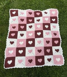 a crocheted blanket with hearts is laying on the grass in front of it