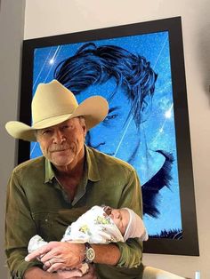 a man holding a baby in front of a cowboy hat and painting on the wall