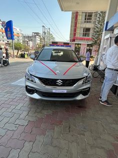 a silver car parked in front of a gas station with two men standing next to it