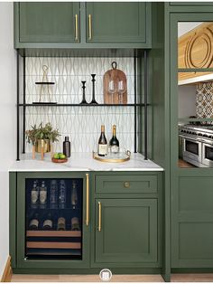 a kitchen with green cabinets and white counter tops, wine bottles on the shelves in front of the sink