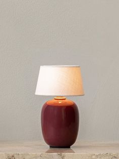 a red lamp sitting on top of a table next to a white light fixture and a wall