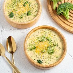 three bowls of broccoli cheese soup with spoons and utensils on the side