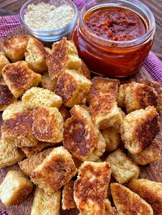 some fried food is sitting on a wooden board next to two small bowls of sauce