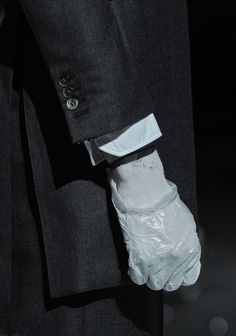 a man in a suit and tie with white gloves on his hand, holding something wrapped in plastic