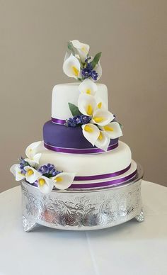 a three tiered wedding cake with purple and white flowers on the top, sitting on a silver platter