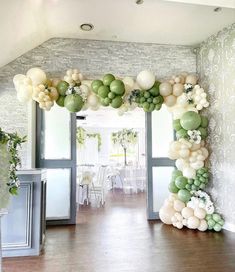 an arch made out of balloons and greenery is displayed in the middle of a room