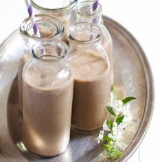 three jars filled with brown liquid sitting on top of a metal plate next to flowers