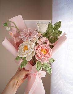 a person holding a bouquet of flowers with pink ribbon and green leaves on the top