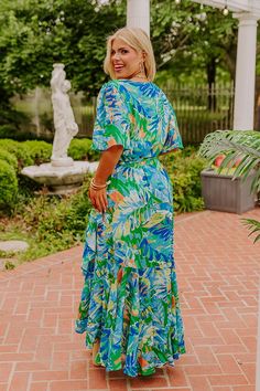 - Paradise is calling with this gorgeous dress! A vibrant botanical print and a wrap style cut give it a seaside chic feel. Wrap yourself in tropical vibes with this eye-catching maxi. - Lightweight material with an abstract botanical print featuring greens, blues, yellows, and orange hues - A built-in lining ending above the knee - A surplice neckline - A wrap style cut with side tie closure at the waistline - Short, loose sleeves - A flowy yet flattering silhouette that ends in an uneven hemli Green Tropical Print Maxi Dress For Garden Party, Tropical Maxi Dress With Vibrant Print For Garden Party, Tropical Short Sleeve Maxi Dress For Beach Cover-up, Tropical Floral Print Maxi Dress With Short Sleeves, Tropical Floral Print Short Sleeve Maxi Dress, Tropical Short Sleeve Printed Maxi Dress, Tropical Printed Maxi Dress With Short Sleeves, Blue Tropical Print Maxi Dress For Beach Party, Tropical Maxi Dress With Tropical Print For Garden Party