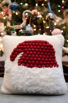 a red and white knitted pillow sitting on top of a table next to a christmas tree