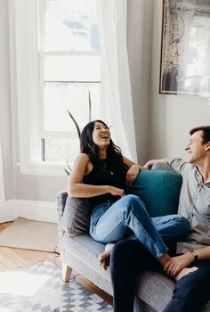 a man and woman sitting on a couch laughing at each other's eyes as they laugh