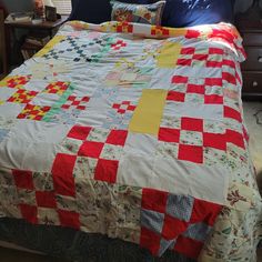 a bed with a red, white and yellow quilt on top of it next to a window