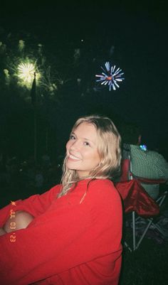 a woman in a red shirt is smiling at fireworks