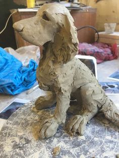 a statue of a dog sitting on top of a piece of pottery in a workshop