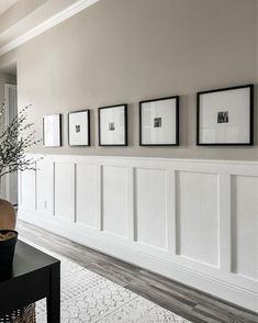 a living room with white paneling and pictures on the wall, along with a vase filled with baby's breath flowers