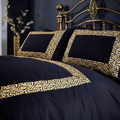 a bed with black and gold comforters in a bedroom next to a vase filled with flowers