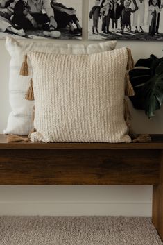 a wooden bench with two pictures on the wall above it and a white throw pillow