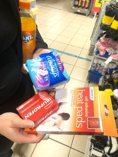 a person holding two packets of toothpaste and an orange juice in a store