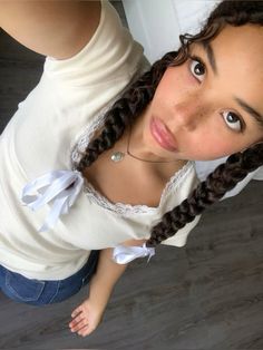 a girl with braids and a white shirt is looking up at the camera while holding her cell phone