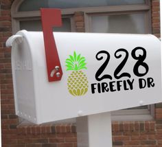 a white mailbox with a pineapple decal on it's side in front of a brick building