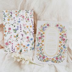 the wedding stationery is laid out next to each other on a white sheet with flowers