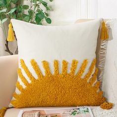 a yellow and white pillow sitting on top of a couch next to a plant in a vase