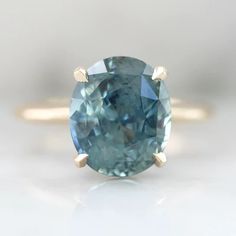 an oval cut blue diamond with two gold accents on the band, sitting on a white surface