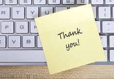 a sticky note attached to a keyboard with the words thank you written on it in black ink