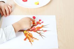 a child's hand holding a paintbrush over a piece of paper that is on top of a table