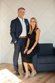 a man and woman standing next to each other in front of a blue couch, smiling at the camera