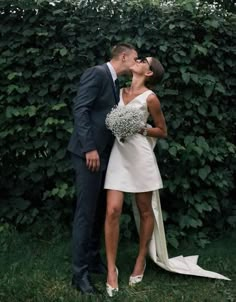 a bride and groom kissing in front of a hedge