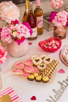 valentine's day dessert table with pink flowers, cookies and bottles of wine in the background