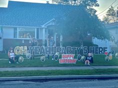 two people sitting on the grass in front of a house with a sign that says oh yeah party is here