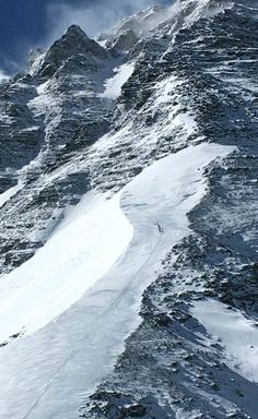 a man riding skis down the side of a snow covered mountain under a cloudy blue sky