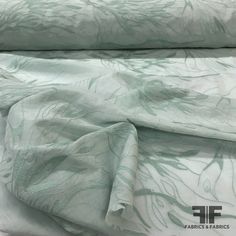 an image of a bed with white sheets and green leaves on it's cover