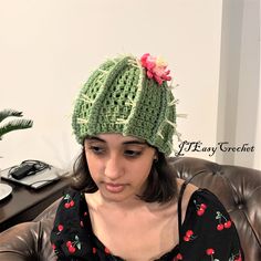 a woman wearing a green crocheted hat with flowers on it sitting in a chair