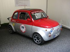 a small silver and red car parked in a garage next to a white wall with writing on it